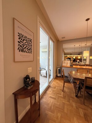 A modern interior with a dining area, a large framed artwork on the wall, and a view into the adjacent room.