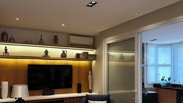 A modern living room with a sofa, ottoman, and a television. There is a kitchen area visible through a glass door. - Copacabana 3BR • 1 Block to the Beach — Stylish & Family-Friendly (Rio de Janeiro)