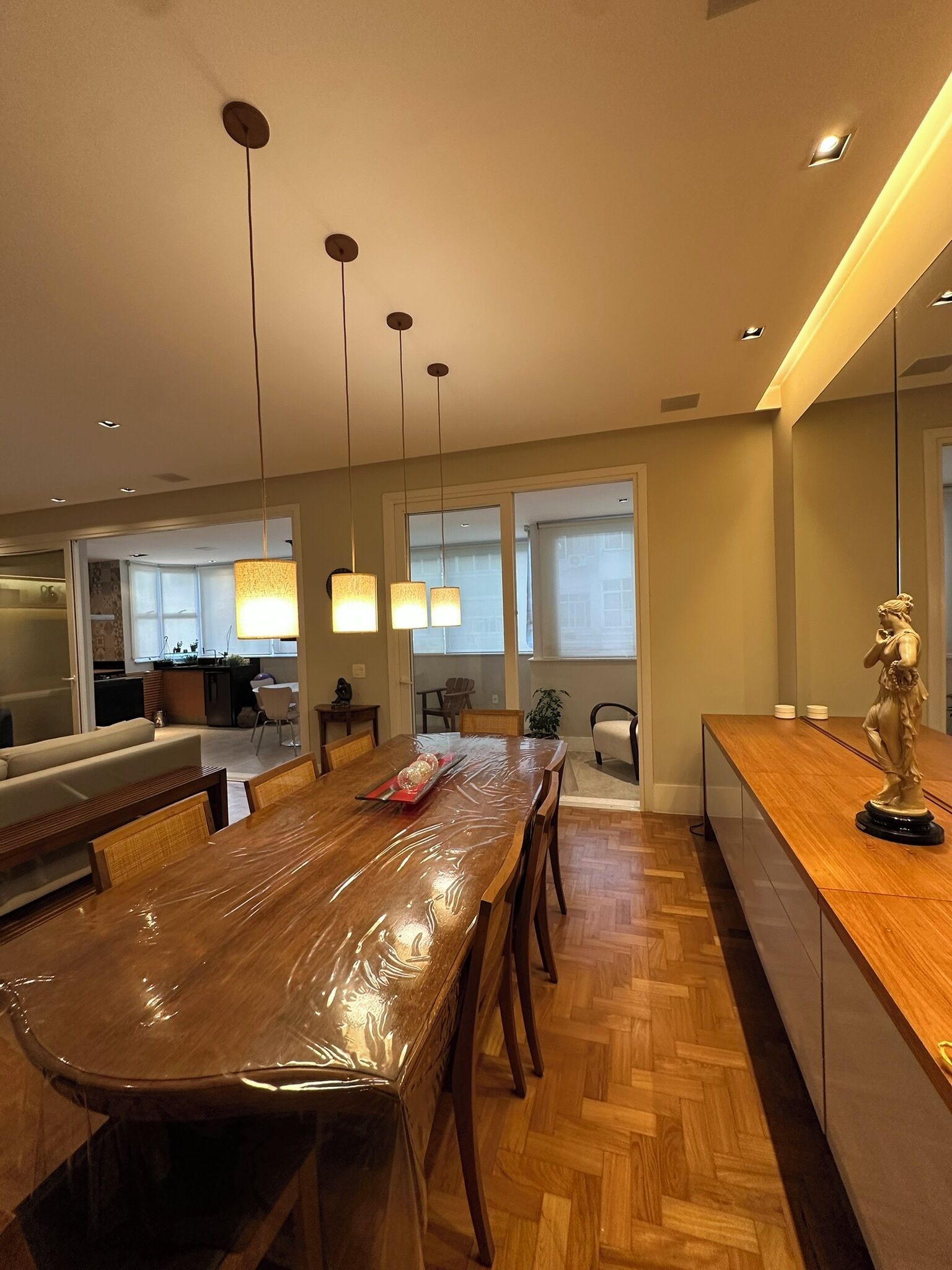 Un comedor moderno con una mesa de madera cubierta con plástico, rodeada de sillas y una estatua en la encimera.