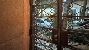 A wrought iron gate with glass panels, leading to a tiled area with a view of parked cars and a building in the background. - Copacabana 3BR • 1 Block to the Beach — Stylish & Family-Friendly (Rio de Janeiro)
