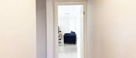 A hallway leading to a living area with a dark blue sofa and a small table with a plant.