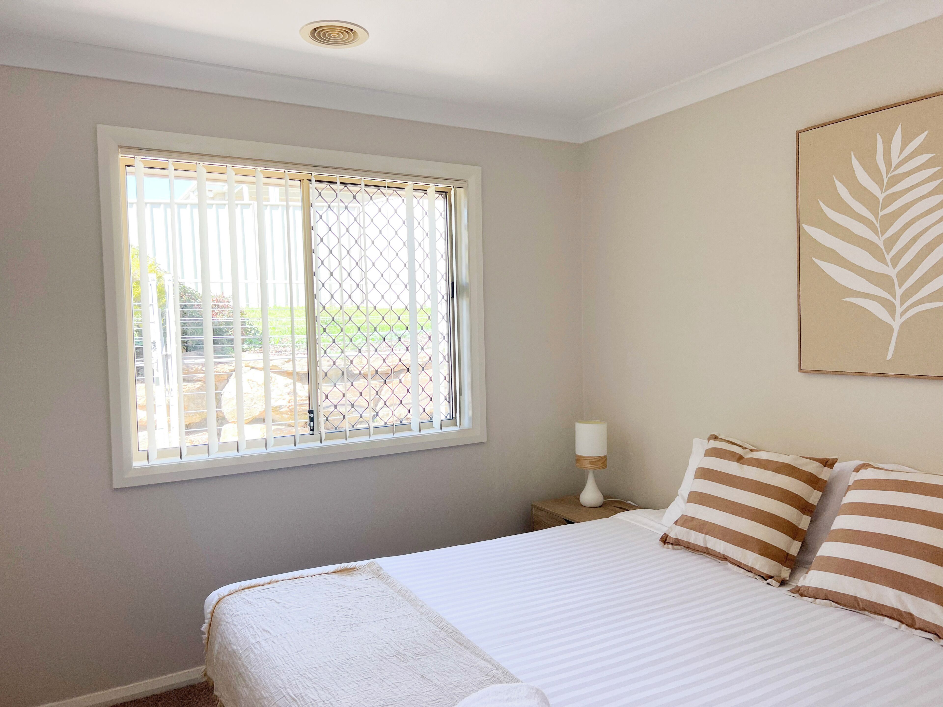 Ein Schlafzimmer mit Bett, Fenster mit Blick, Nachttisch und einem Wandbild.