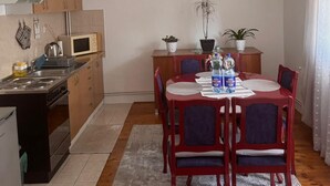 A compact kitchen with a dining area, featuring a microwave, stove, and cabinets. There are potted plants and a dining table with chairs. - Alea Place (Sarajevo)