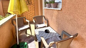 A small balcony with a table and chairs, a green mat, and a potted plant on the windowsill. - Alea Place (Sarajevo)