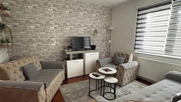 A living room with a stone wall, a television on a stand, a sofa, and a coffee table. - Alea Place (Sarajevo)