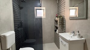 A modern bathroom with a glass-enclosed shower, a toilet, a sink with a mirror, and a small window. - Alea Place (Sarajevo)