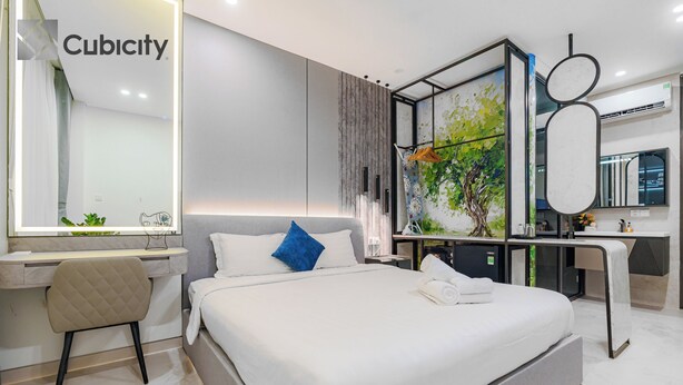 A modern hotel room with a large bed, a desk, a chair, a mirror, and a wall with a nature-themed artwork. - Cubicity Pho Duc Chinh (Ho Chi Minh Municipality)