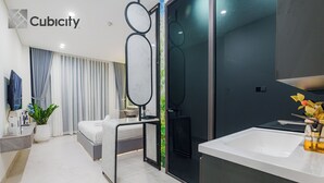 Ein modernes Hotelzimmer mit Bett, Schreibtisch, großem Spiegel, Badezimmer mit Waschbecken und Toilette sowie einem an der Wand montierten Fernseher.