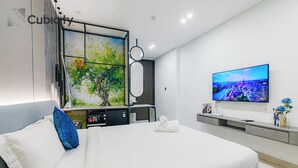 A modern hotel room with a large bed, a flat-screen TV mounted on the wall, and a painting of a tree. - Cubicity Pho Duc Chinh (Ho Chi Minh Municipality)
