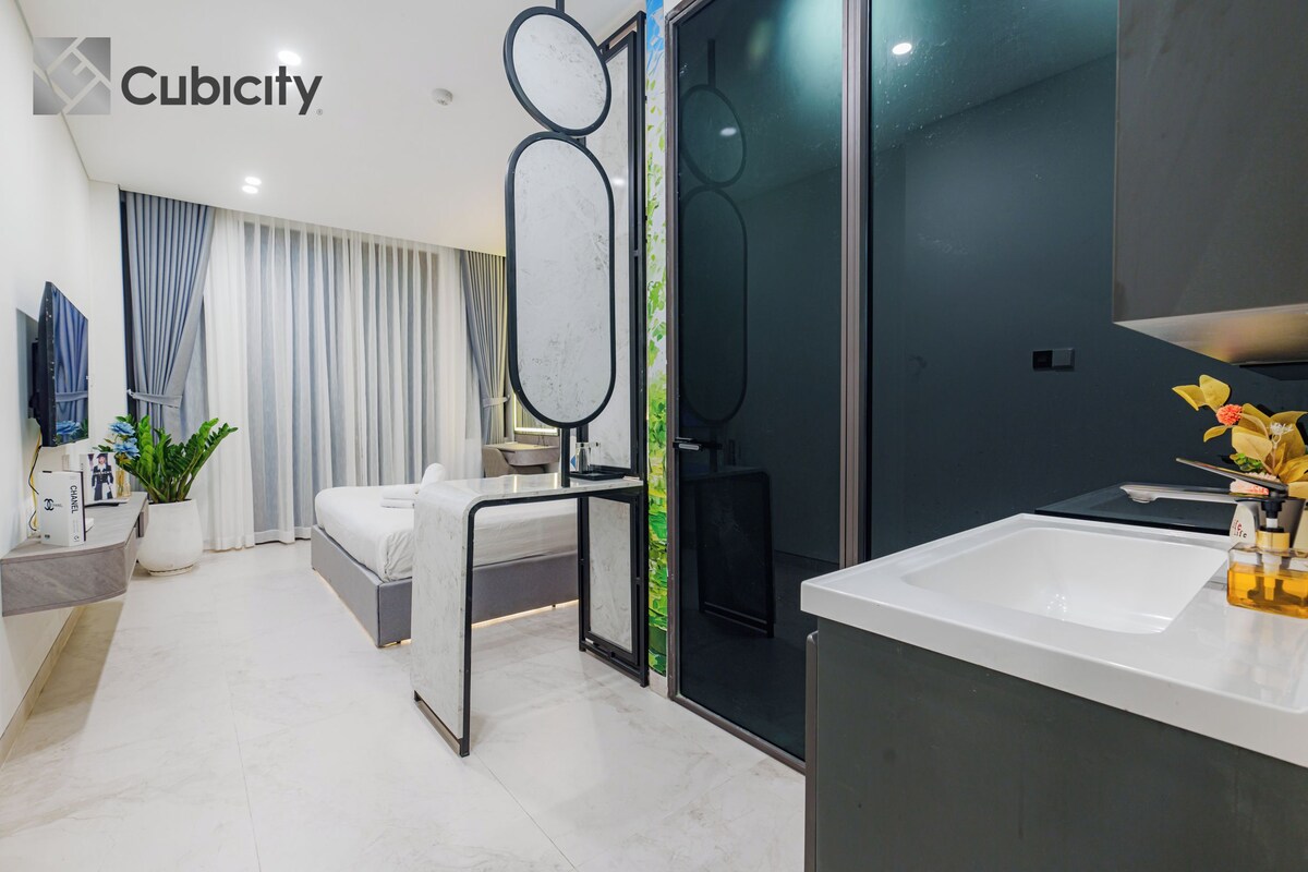 Una habitación de hotel moderna con cama, escritorio, espejo grande, zona de ducha y baño con lavamanos.