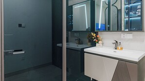 Ein modernes Badezimmer mit Glastür, Waschbecken in Weiß, Spiegel und einer kleinen Vase mit Blumen.