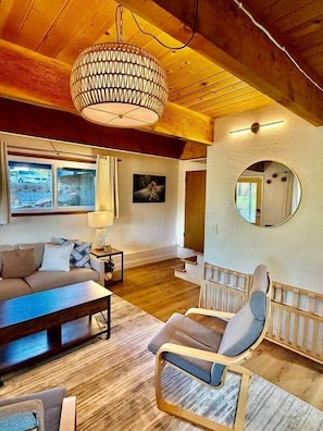 A cozy living room with a sofa, armchair, and coffee table, wooden floors, and a large chandelier.
