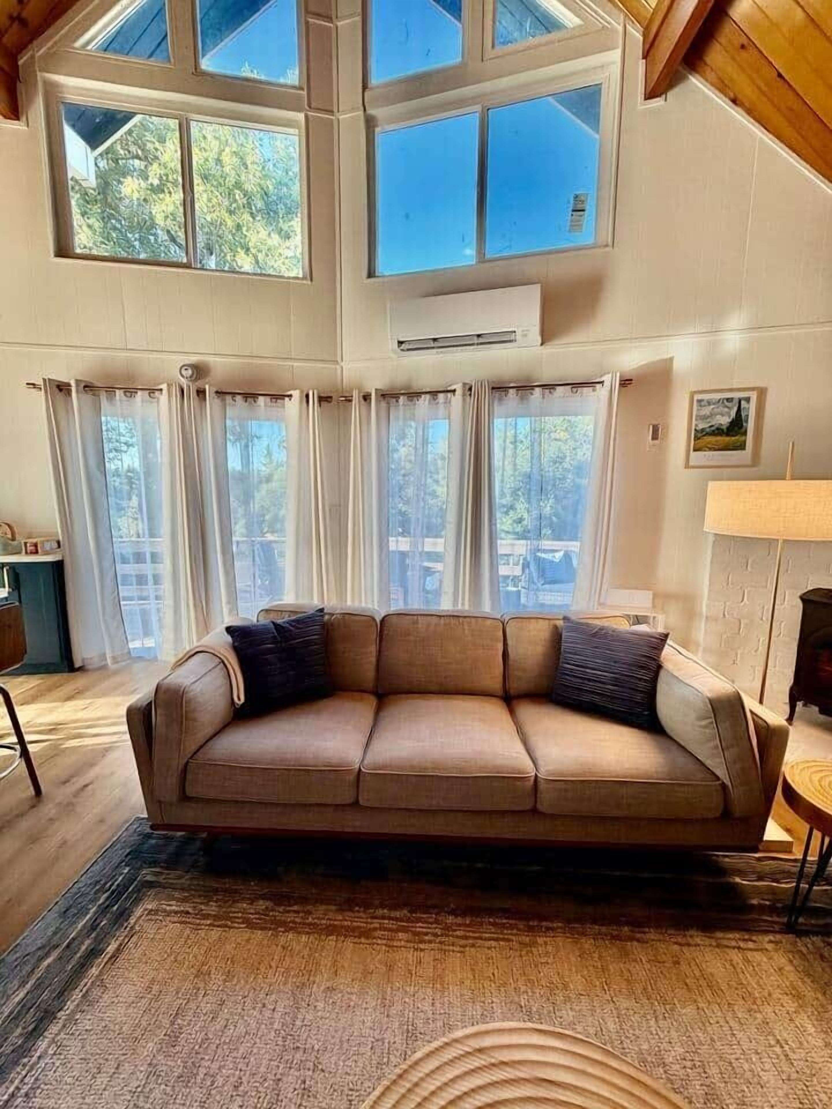 Una habitación con sofá color beige, ventanas amplias y techo de madera.