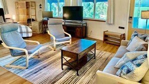 Een houten interieur met een bank, stoelen, een televisie en een raam met gordijnen.