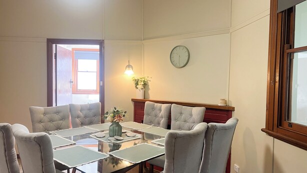 A conference room with a glass table, grey upholstered chairs, a clock on the wall, and a window with a view.