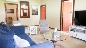 A living room with a blue sofa, a glass coffee table, a grey armchair, and a TV on a white stand.