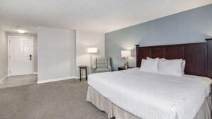 A hotel room with a large bed, a nightstand, a chair, and a door. - Bayside King Ocean Front Island Views (Eastsound)