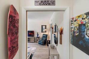 Ein Wohnzimmer mit einem Surfbrett, einem Schild mit der Aufschrift "BAT CAVE", einem Fernseher, der "NETFLIX" zeigt, und einem Batman-Poster.