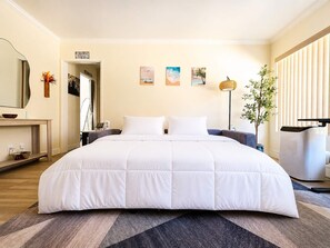 Ein Hotelzimmer mit einem großen Bett, Nachttischen, einem Spiegel, Kunstwerken an der Wand und einer Pflanze.