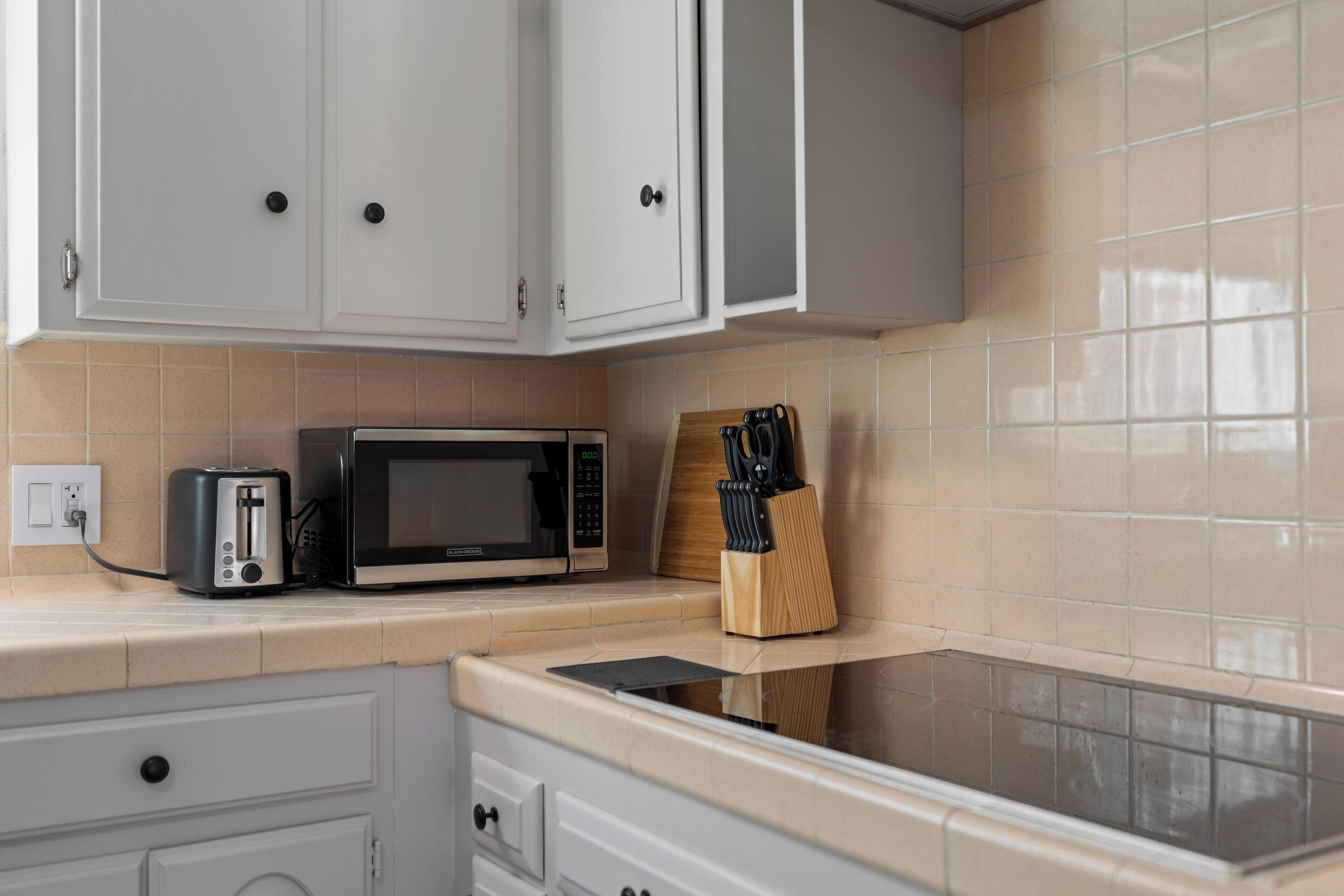 A kitchen with white cabinets, a microwave, a toaster, and a knife block on the countertop.