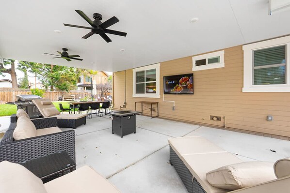 An outdoor patio with wicker furniture, ceiling fans, and a TV mounted on the wall.