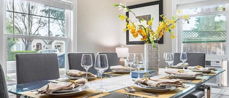 A dining room with a glass table, grey chairs, and a vase of yellow flowers.