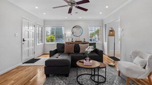 A modern living room with a dark grey sectional sofa, a round mirror, and a ceiling fan. - East SJ Entire 4Br Home Quiet (San Jose)
