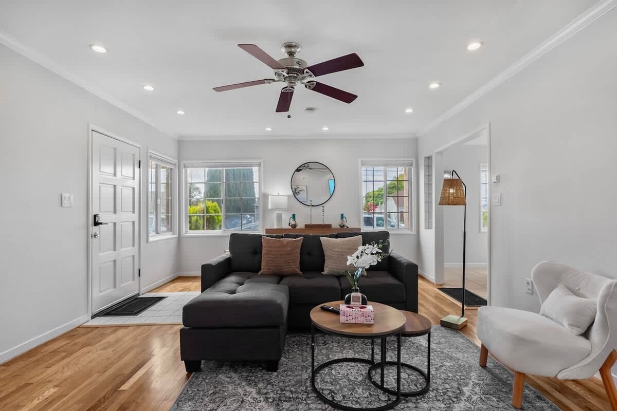 A modern living room with a dark grey sectional sofa, a round mirror, and a ceiling fan.