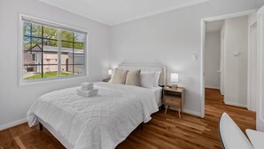 A bedroom with a large window, a bed with white bedding, a nightstand, and a wooden floor. - East SJ Entire 4Br Home Quiet (San Jose)