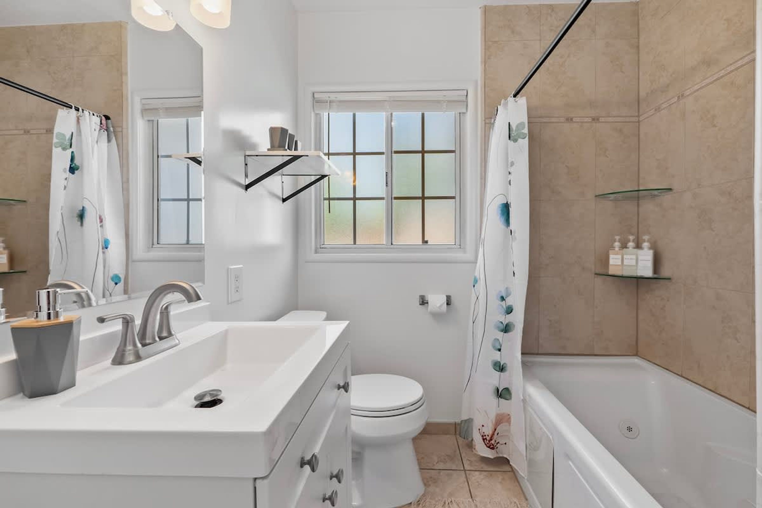 A modern bathroom with a white sink, a toilet, a shower with a curtain, and a window with a view.