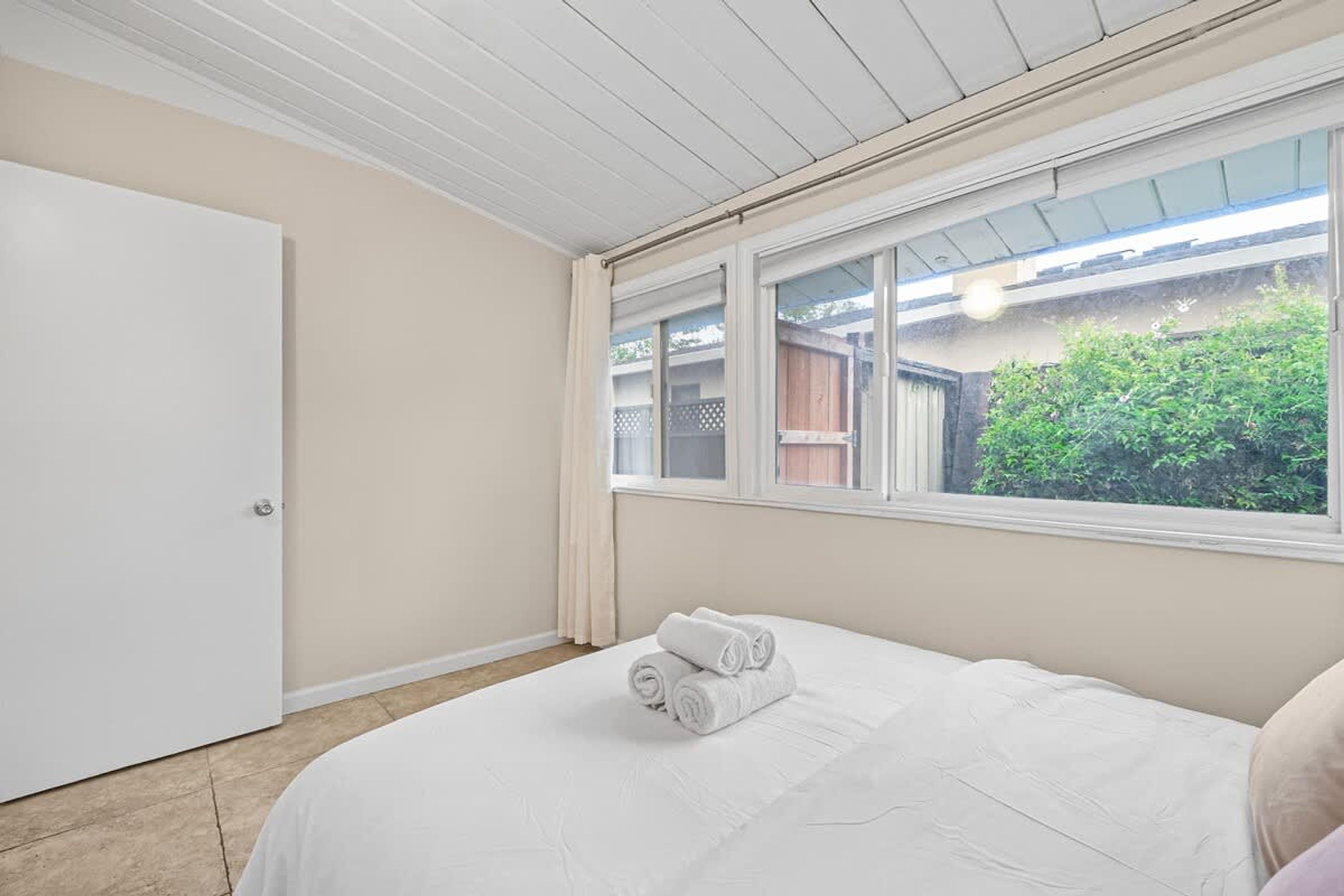 A bedroom with a large window, a bed with white bedding, and a door.