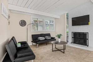 A living room with a black sofa, a coffee table, a fireplace, and a wall-mounted TV. - Entire 3br House With Playground (Palo Alto)