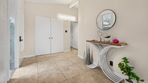 A hallway with a white door, a mirror, and a shelf with decorative items. - Entire 3br House With Playground (Palo Alto)