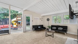 A spacious living area with a sliding glass door leading to a backyard, a black sofa set, a coffee table, and a flat-screen TV mounted on the ceiling. - Entire 3br House With Playground (Palo Alto)