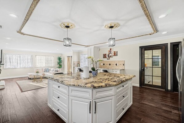 A spacious kitchen with a large island, white cabinetry, and pendant lighting.