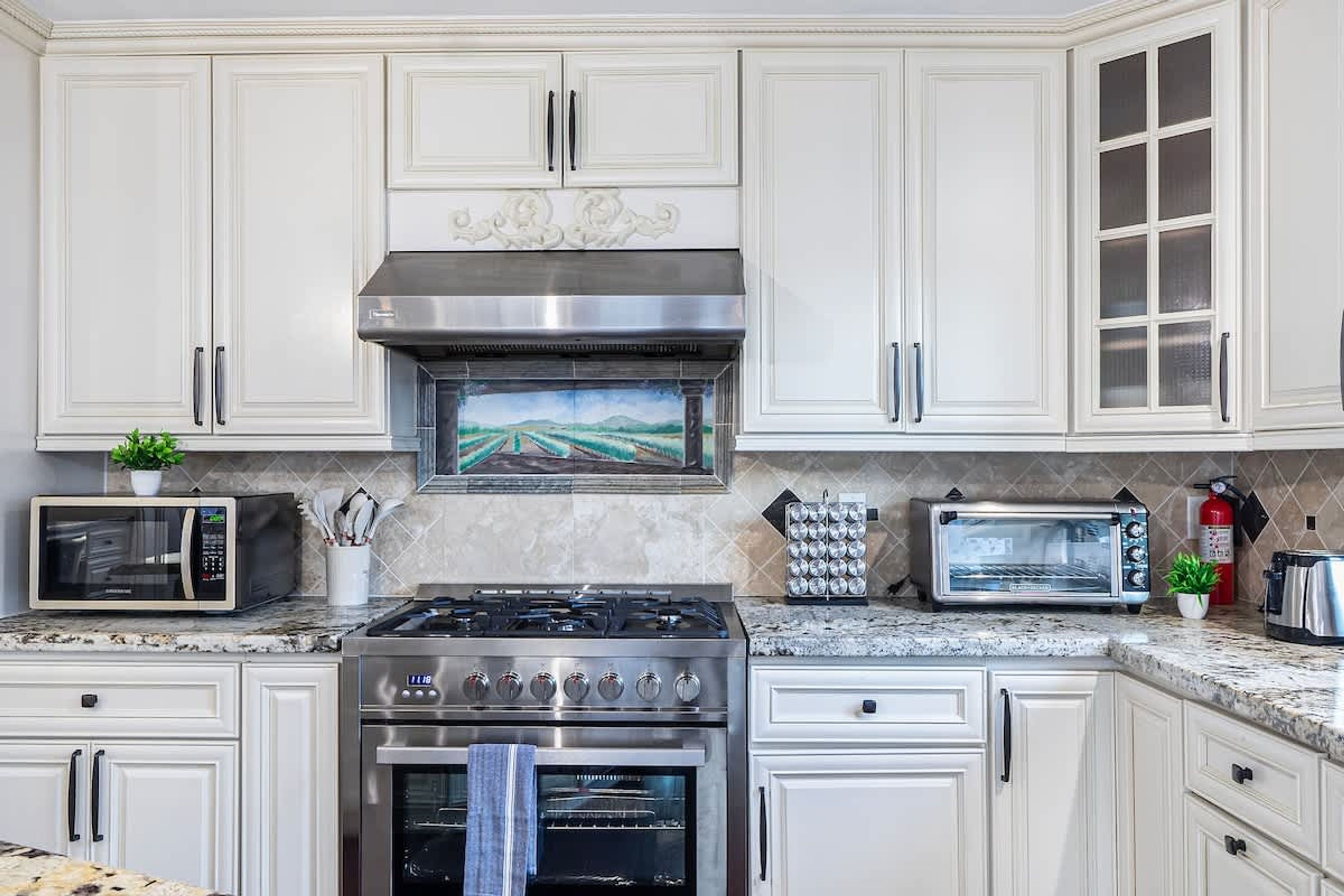 A kitchen with white cabinets, a stainless steel range hood, a microwave, a toaster, and a gas stove.
