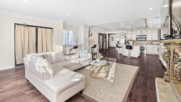 A spacious living room with a large white sofa, a round coffee table, and a kitchen area with white cabinets and a large island. - Stunning Roman Design 7bed5bath in Heart San Jose (San Jose)