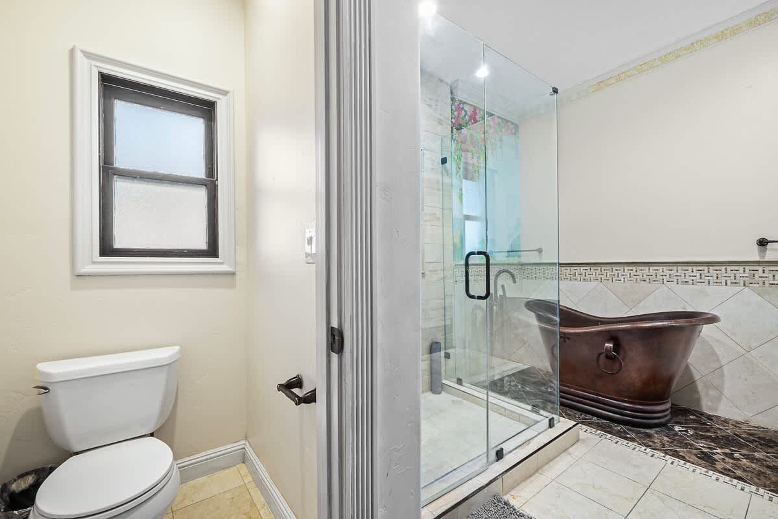 Ein Badezimmer mit Toilette, einer in Glas abgeschirmten Dusche und einer Badewanne im Vintage-Stil.