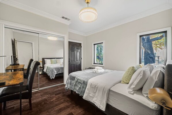 A bedroom with a bed, a desk, and a chair. There is a door leading to another room.