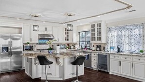 A modern kitchen with white cabinetry, a central island with bar stools, stainless steel appliances, and pendant lighting.