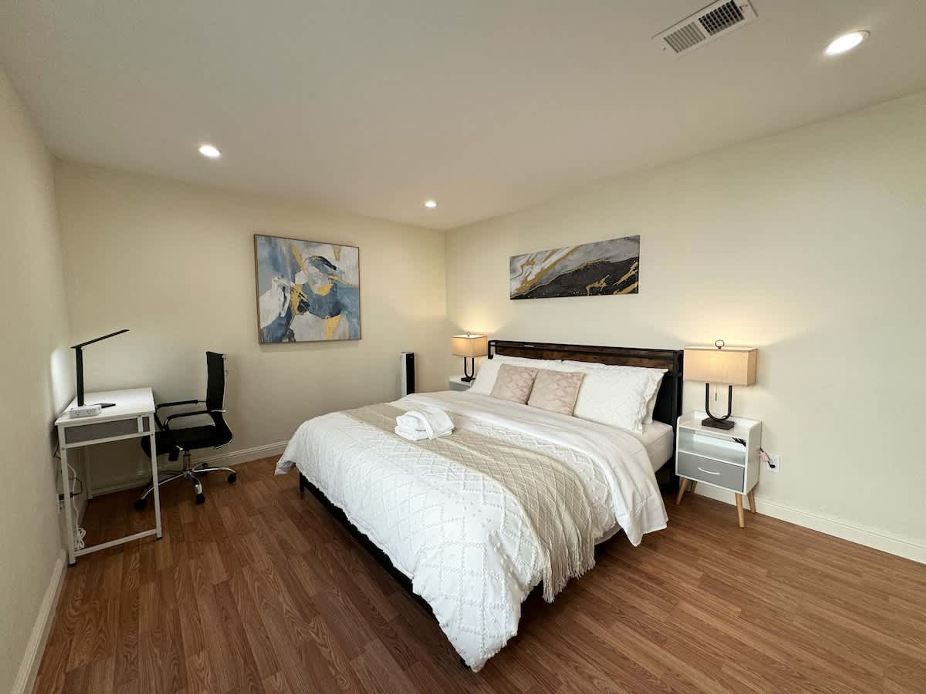 A bedroom with a large bed, two bedside tables, a desk, and two lamps.