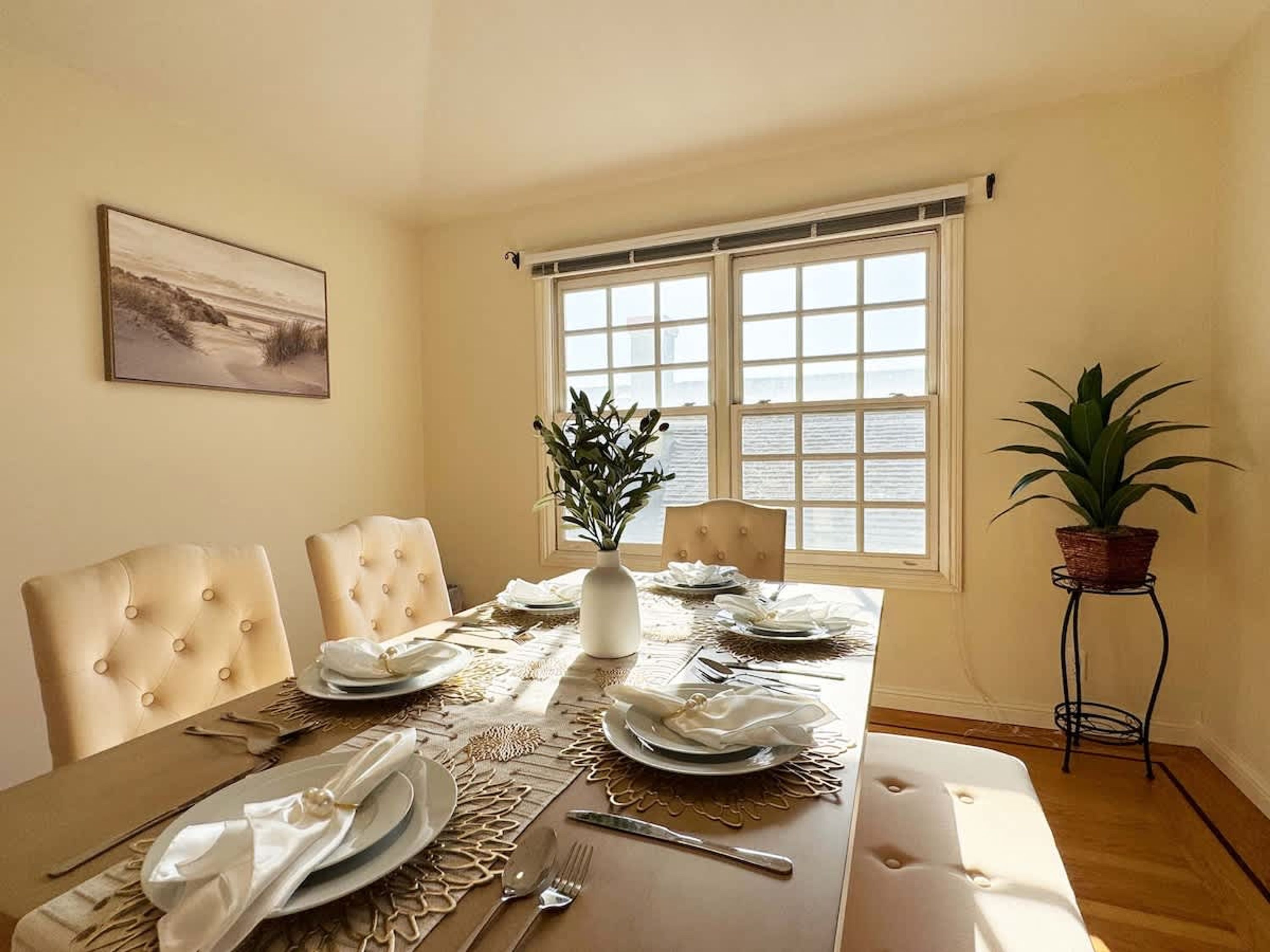 Ein Esszimmer mit Tisch für vier Personen, einem Topf mit Pflanze und Meerblick durch ein Fenster.
