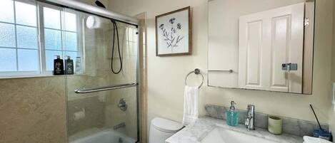 A bathroom with a glass shower enclosure, a white toilet, a marble sink, and a large mirror above the sink.