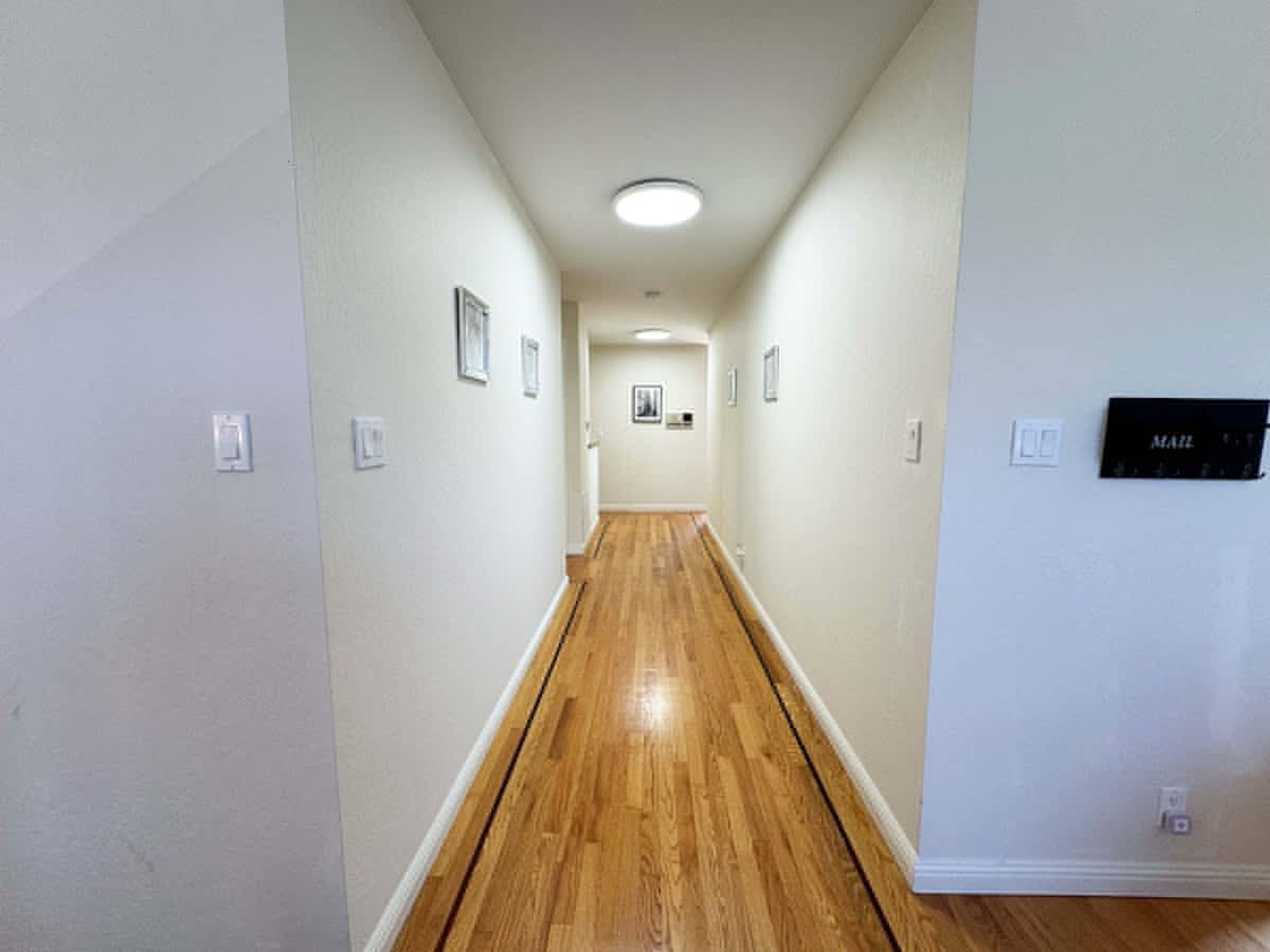 A hallway with wooden flooring, white walls, and a ceiling light.