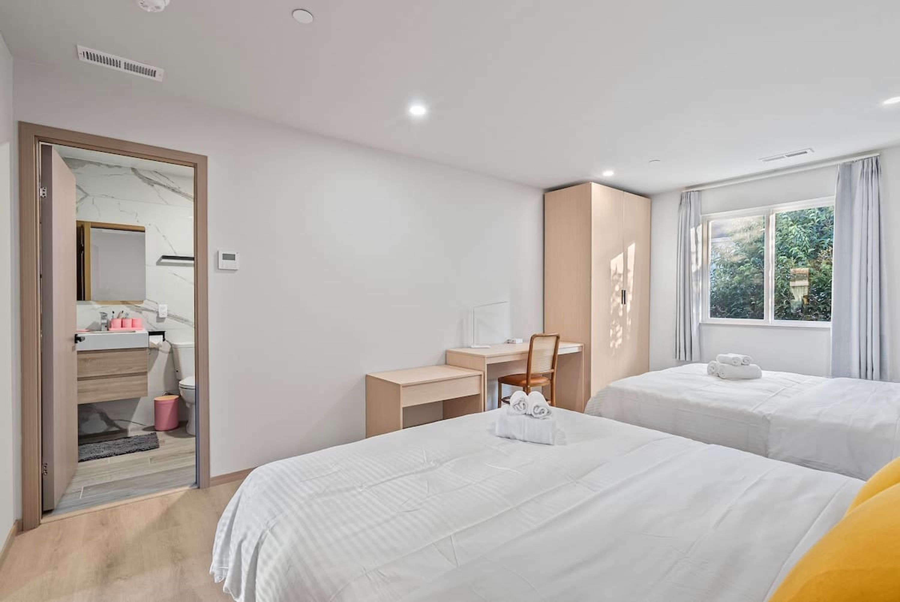 Une chambre d’hôtel avec deux lits, un bureau, une chaise, un miroir et une fenêtre avec des rideaux.