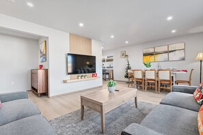 Un salon moderne doté d’un téléviseur à écran plat, de canapés gris, d’une table basse en bois et d’un coin repas avec des chaises et une table en bois.
