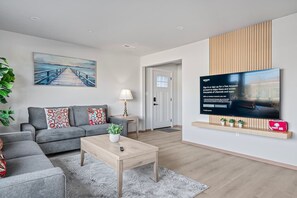 Un salon moderne avec un canapé gris, une table basse et un tableau représentant une jetée. Un téléviseur est fixé au mur et affiche le logo d’Amazon.