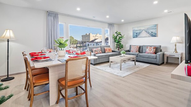 Uma sala de estar moderna com área de jantar, sofás cinza, uma mesa de centro e uma grande janela com vista para a cidade.