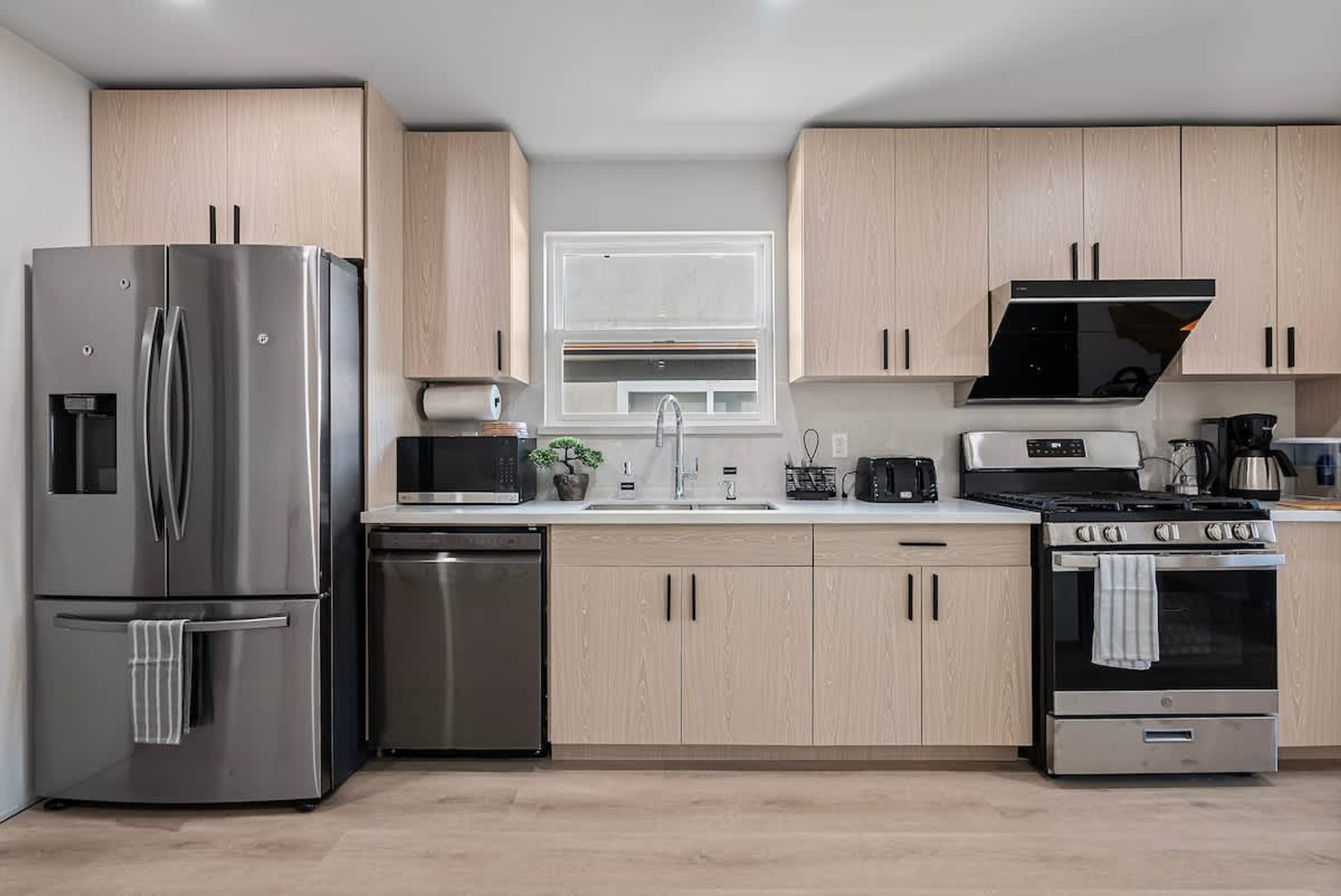 A modern kitchen with stainless steel appliances, light wood cabinets, and a window above the sink.