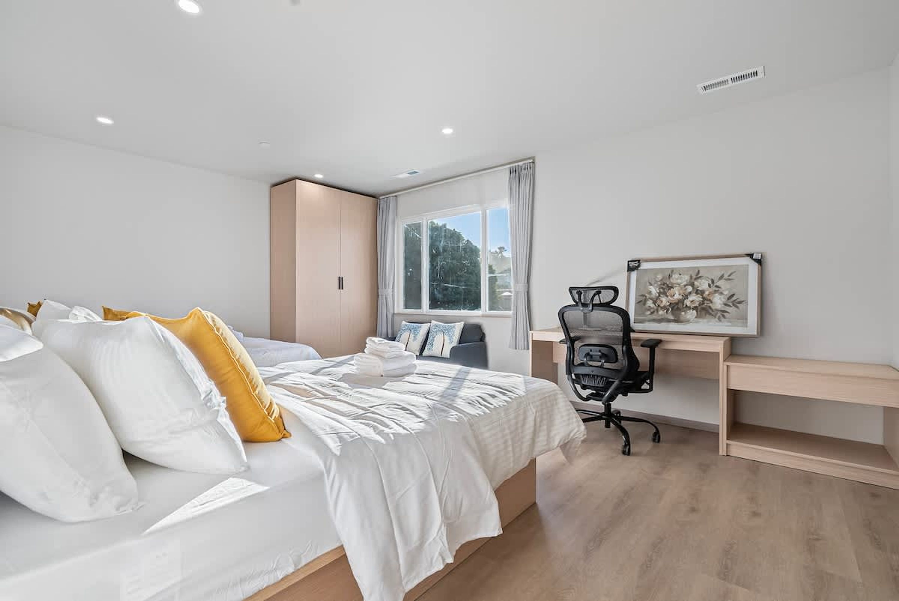 A modern bedroom with a large bed, a desk, and a window with curtains.